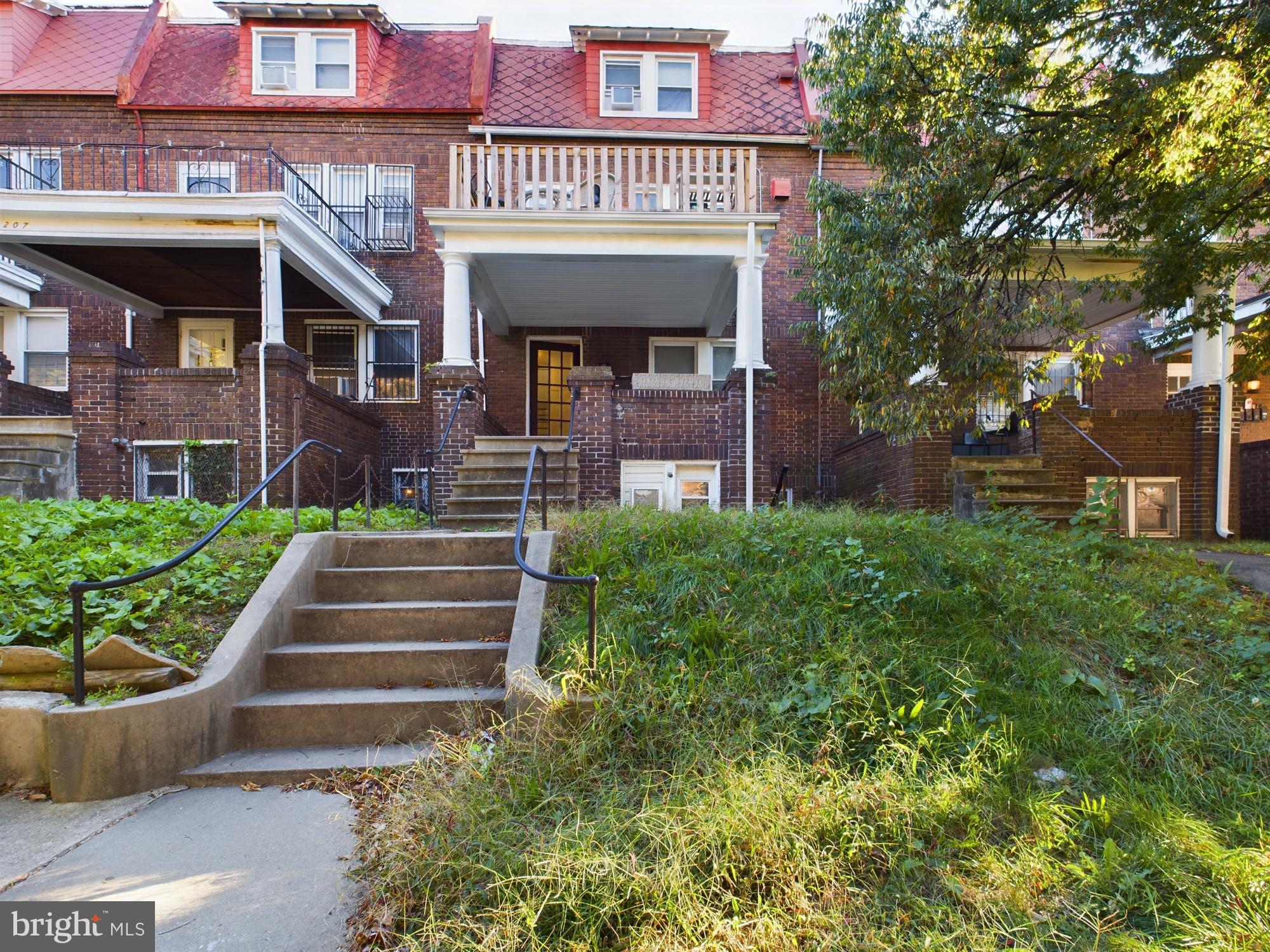 a view of a brick house with a small yard plants and large tree