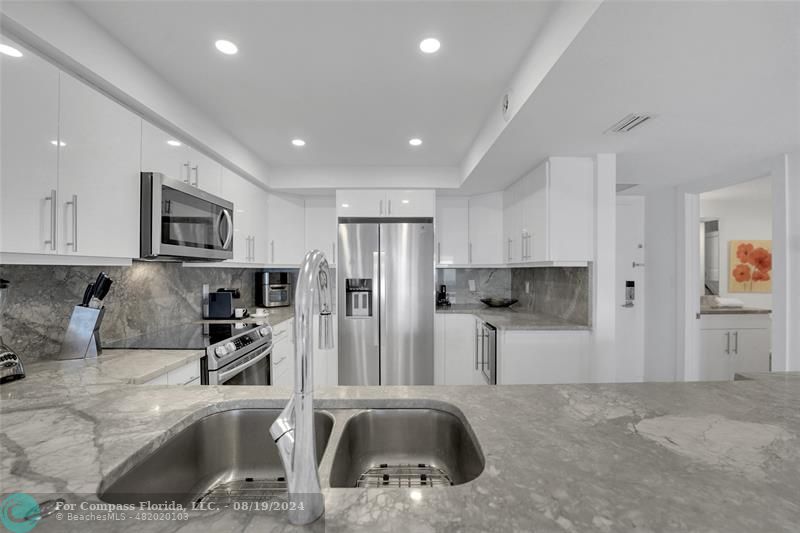 a kitchen with stainless steel appliances kitchen island granite countertop a refrigerator and a sink