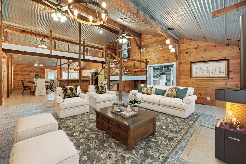 This is a spacious living area with a rustic charm, featuring wooden walls and a corrugated metal ceiling. It includes an open loft space above. The room is well-lit and has a warm, inviting atmosphere.