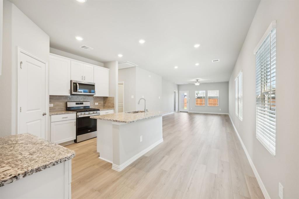 a kitchen with a sink dishwasher stove and white cabinets with wooden floor