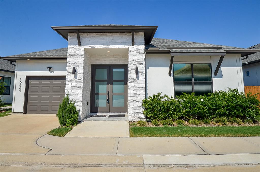 Modern single-story home with a clean-lined aesthetic, featuring a stone accent entryway, prominent front door, and an attached garage.