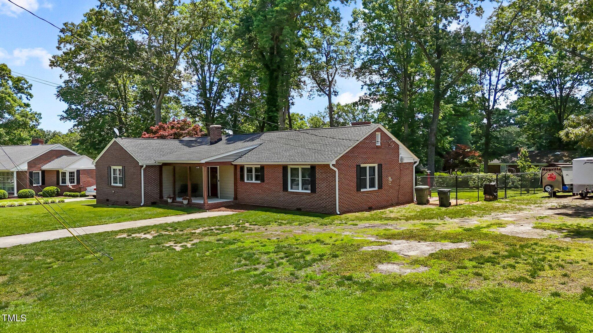 a house that is sitting in the grass with large trees and plants