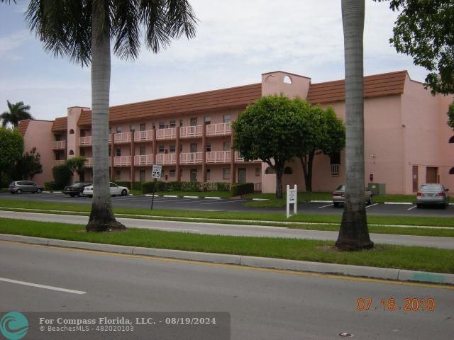 a front view of a building with a garden and trees