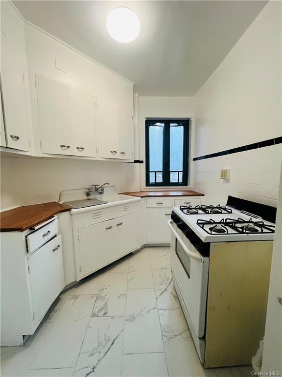 Kitchen featuring white gas stove, sink, backsplash, and white cabinetry