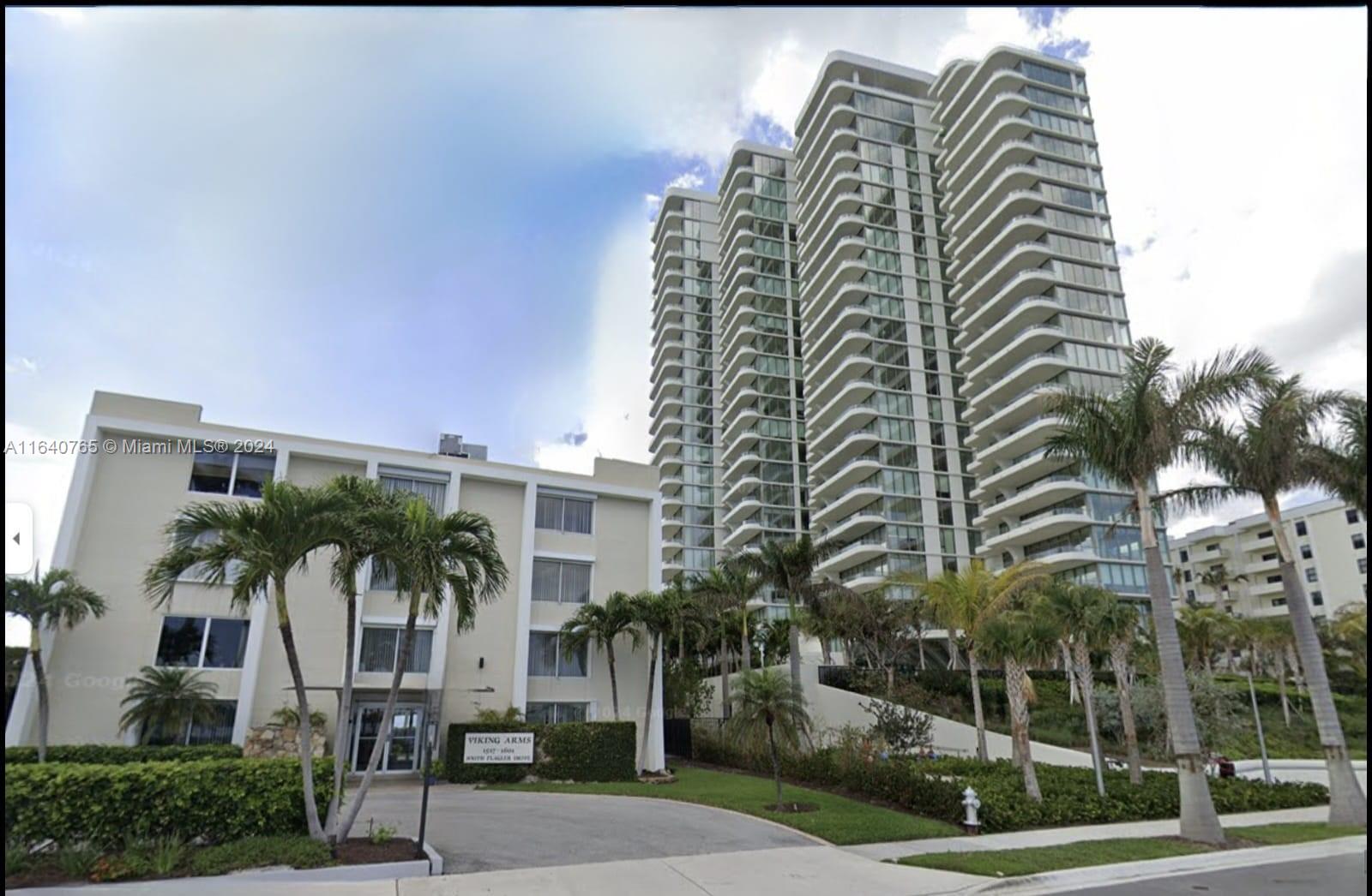 a front view of multi story residential apartment building with yard and sign board