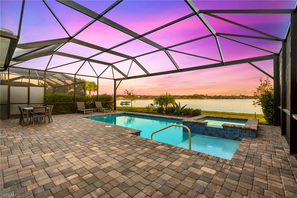 Pool at dusk with a lanai, an in ground hot tub, a water view, and a patio