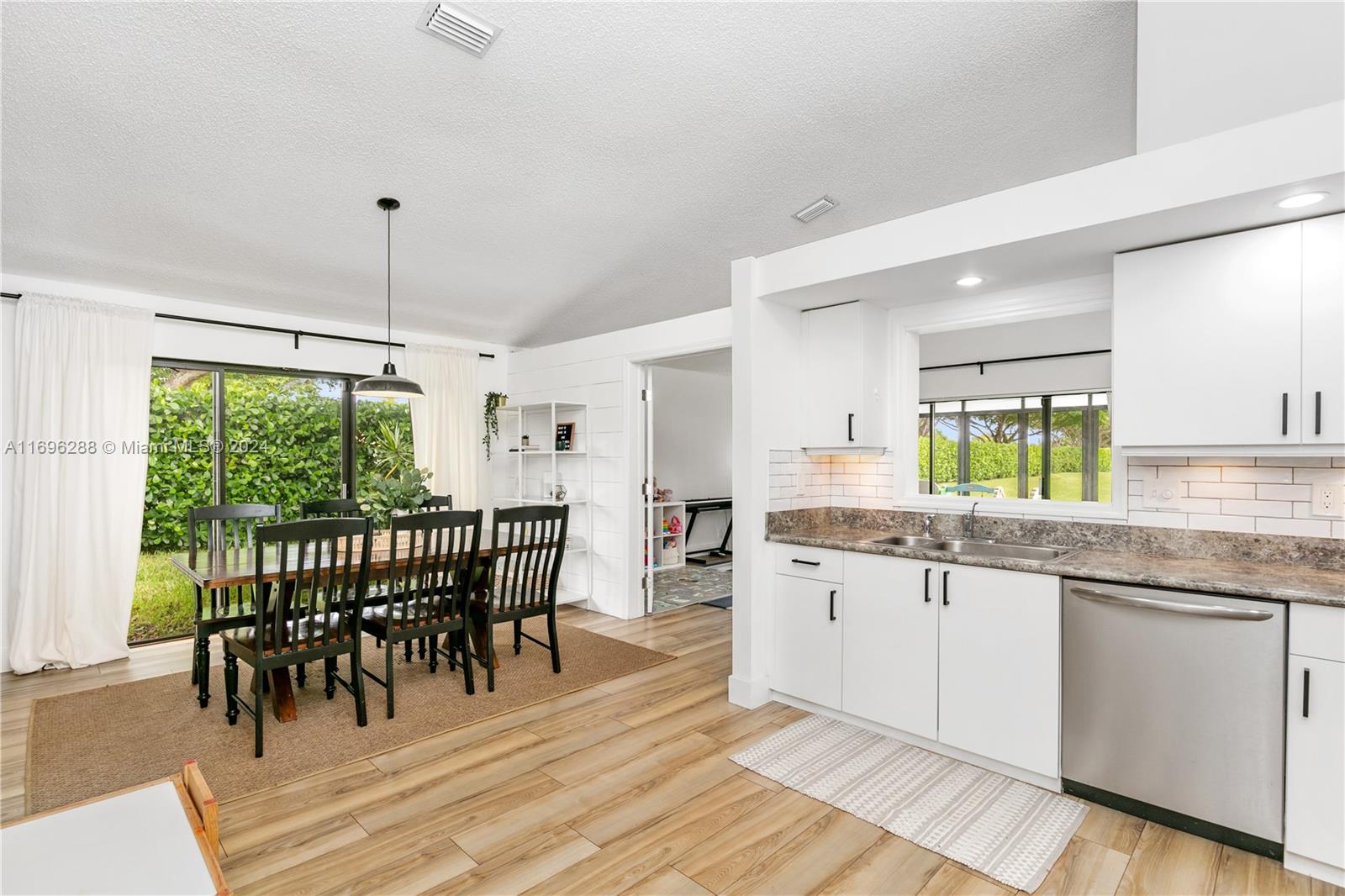 a kitchen with stainless steel appliances granite countertop a dining table chairs sink and white cabinets