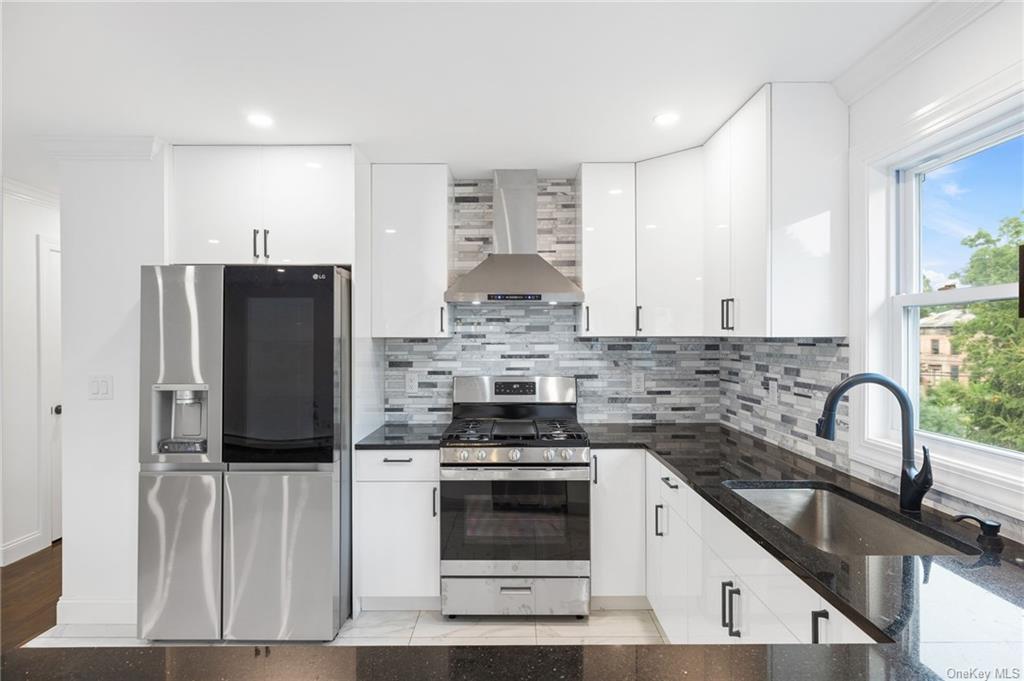 Kitchen with wall chimney range hood, appliances with stainless steel finishes, tasteful backsplash, and a wealth of natural light