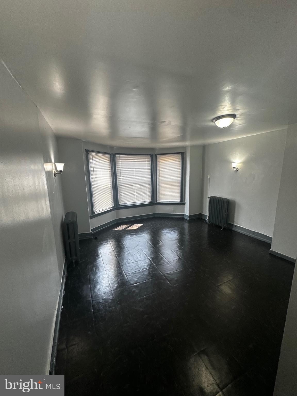 an empty room with wooden floor and windows with curtains