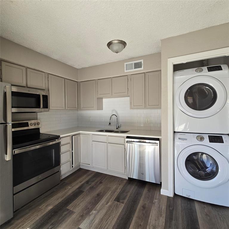 Kitchen with sink, dark hardwood / wood-style flooring, backsplash, stacked washer and dryer, and appliances with stainless steel finishes