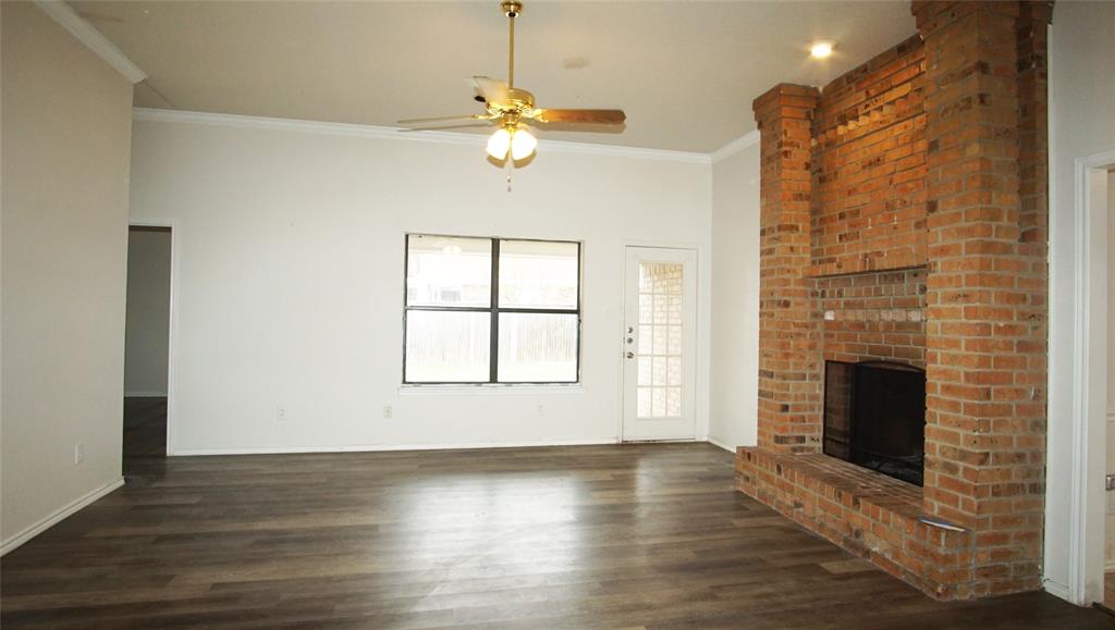 Unfurnished living room featuring dark hardwood / wood-style floors, a brick fireplace, ceiling fan, and ornamental molding