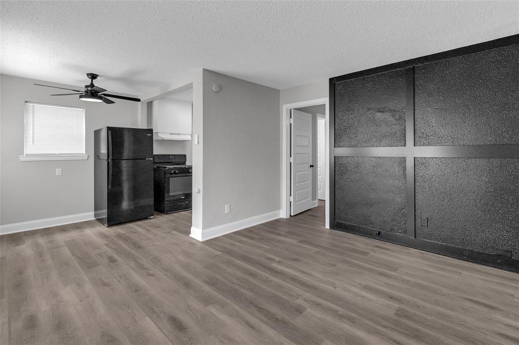 a view of an empty room with wooden floor and a kitchen