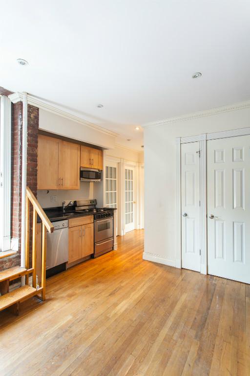 a large kitchen with stainless steel appliances wooden floor and a window