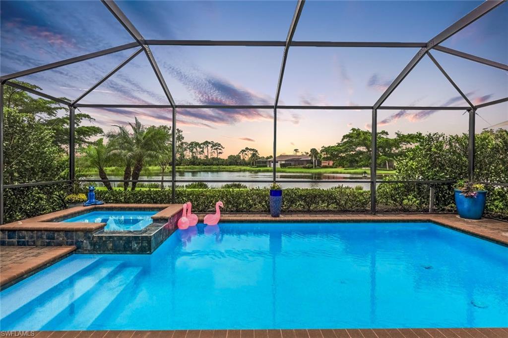 Pool at dusk with a water view, a lanai, and an in ground hot tub