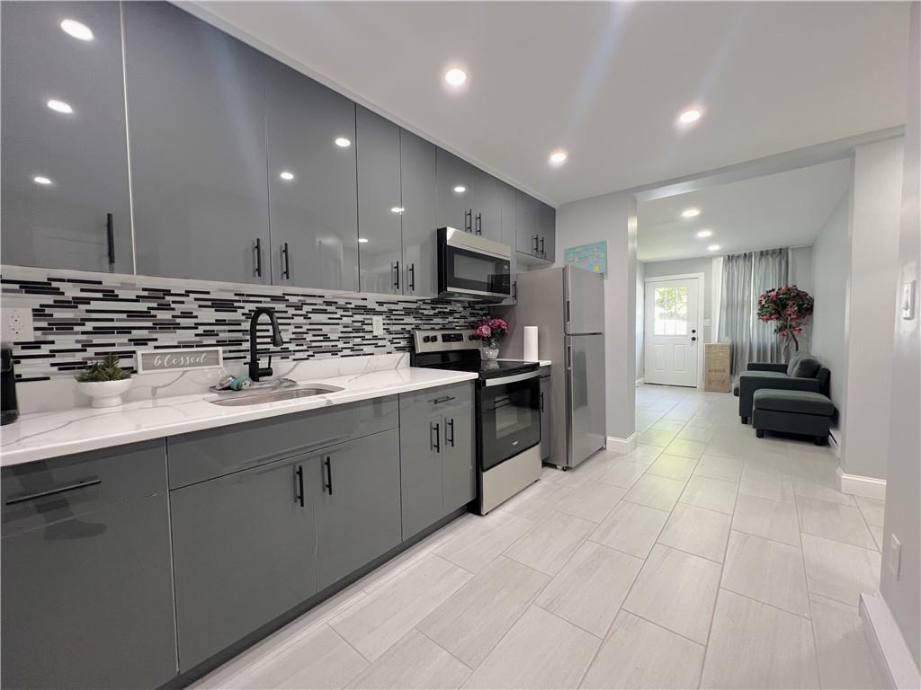 Kitchen featuring appliances with stainless steel finishes, sink, light stone countertops, and backsplash