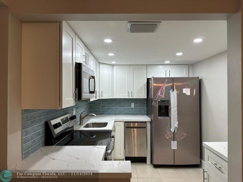 a kitchen with stainless steel appliances granite countertop a refrigerator a stove and a sink with wooden floor