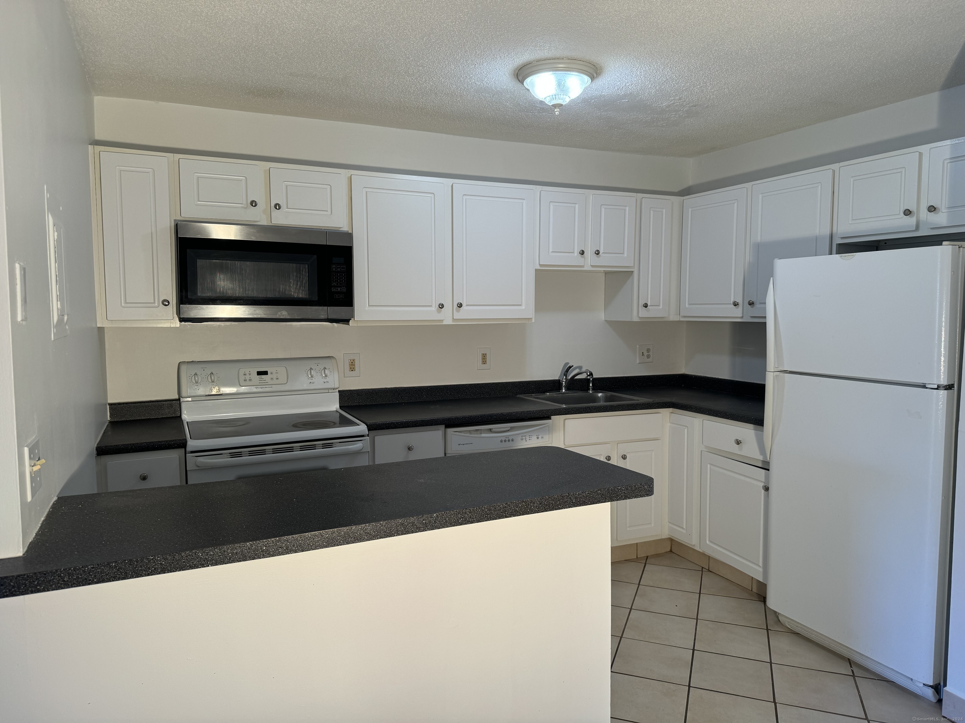 a kitchen with granite countertop a refrigerator sink and white cabinets