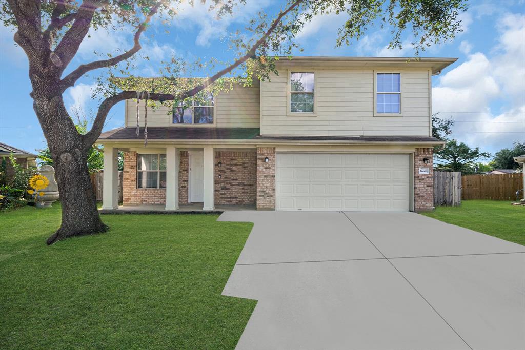 This is a two-story home with a beige siding exterior, brick accents. A mature tree adds charm to the front yard, which is well-manicured.