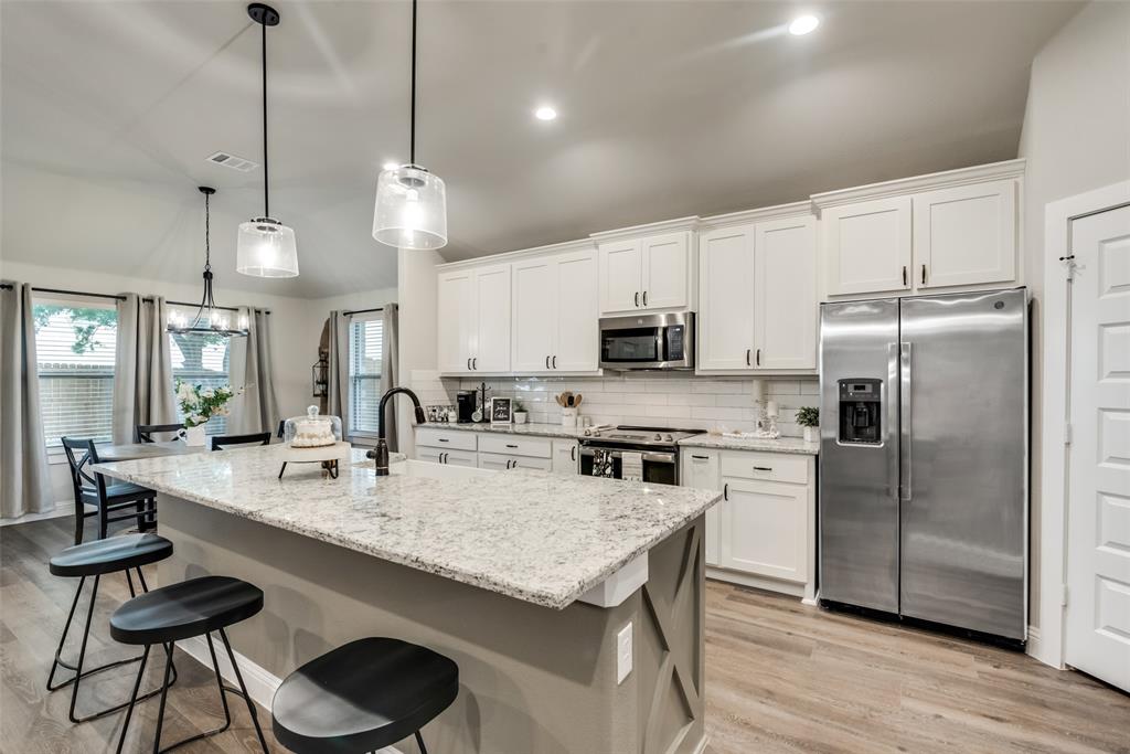 a kitchen with stainless steel appliances granite countertop a stove a refrigerator a kitchen island a sink dishwasher a dining table and chairs with wooden floor