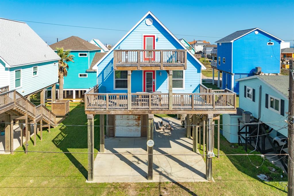 Meet 126 Beachcomber beach-style home features bright blue siding, a spacious front deck, and a second-floor deck. It offers covered parking underneath and is situated in a coastal neighborhood with nearby homes.