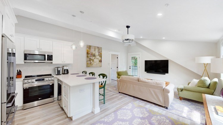 a living room with stainless steel appliances a kitchen island furniture a flat screen tv and a window