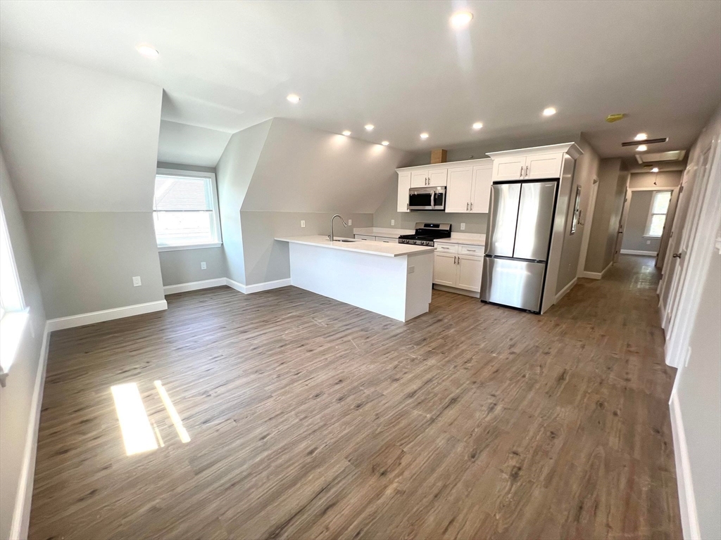 a view of kitchen with stainless steel appliances kitchen island wooden floors and white cabinets