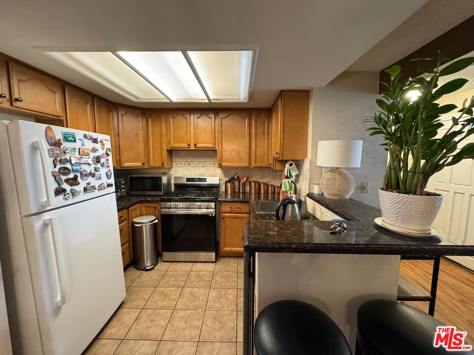 a kitchen with stainless steel appliances granite countertop a refrigerator a sink a stove and a refrigerator