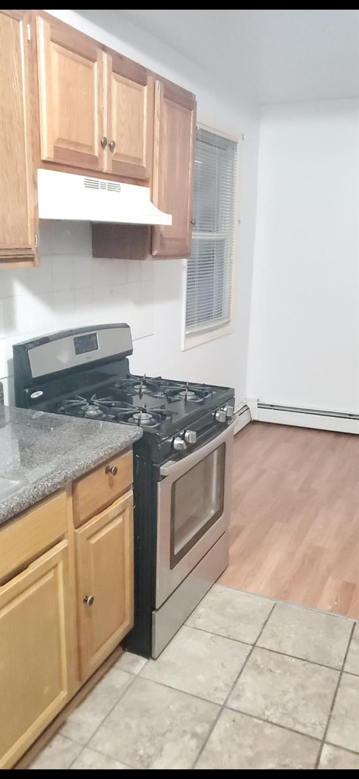 Kitchen with tasteful backsplash, a baseboard heating unit, light hardwood / wood-style flooring, dark stone countertops, and stainless steel range with gas cooktop