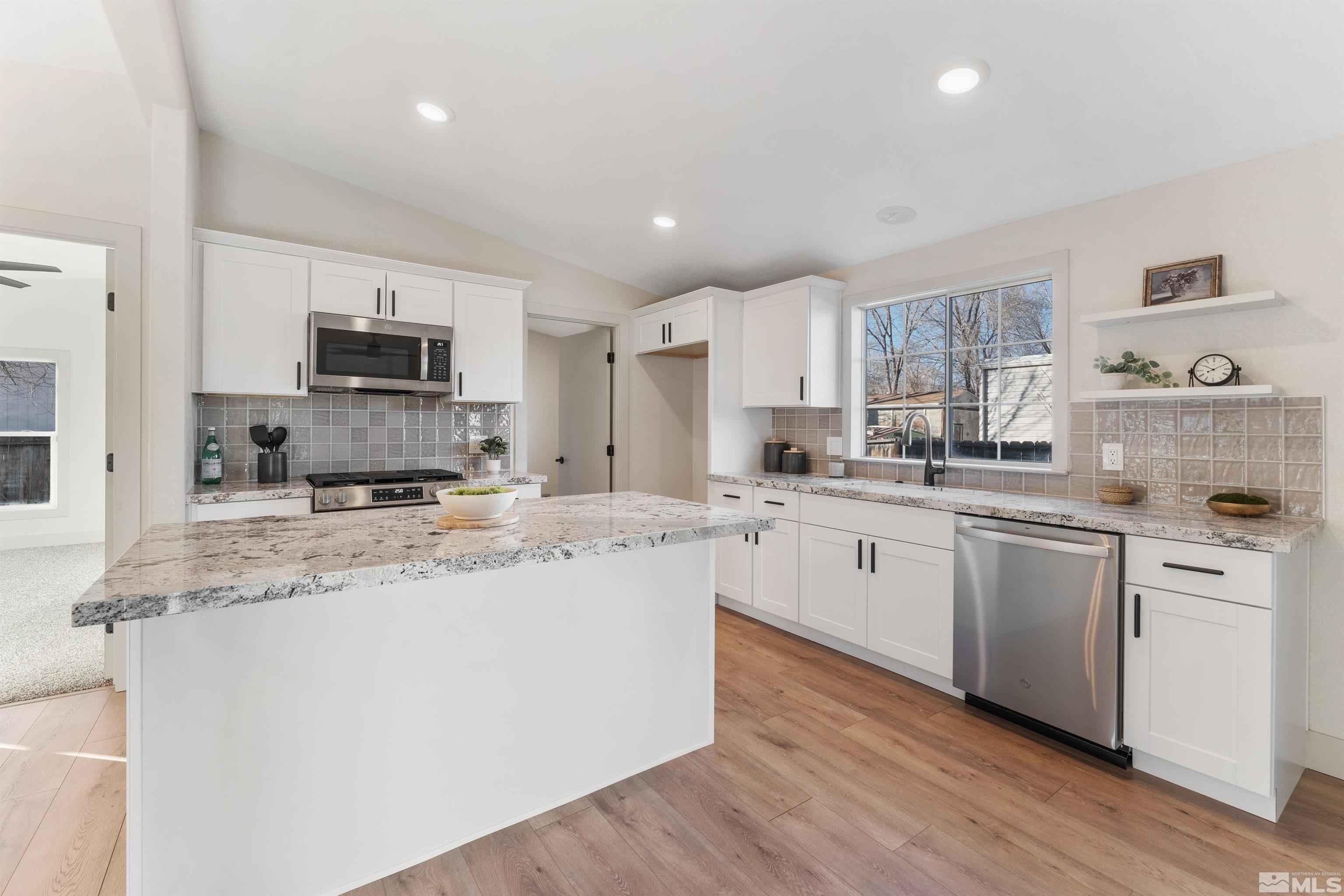 a kitchen with stainless steel appliances granite countertop a sink a stove a refrigerator and white cabinets