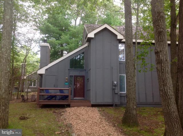 a view of a wooden house with a small yard and a large tree