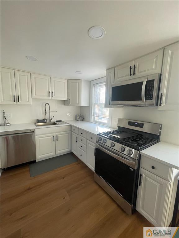 a kitchen with stainless steel appliances white cabinets a sink a stove a microwave and wooden floors