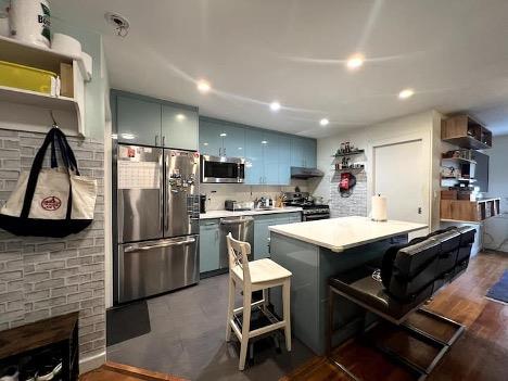 Kitchen with a breakfast bar, backsplash, dark hardwood / wood-style flooring, kitchen peninsula, and stainless steel appliances