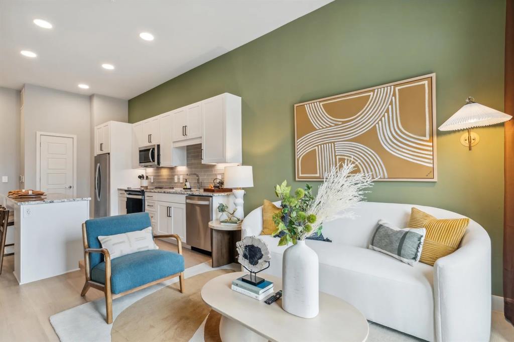 a living room with stainless steel appliances furniture a rug and a kitchen view