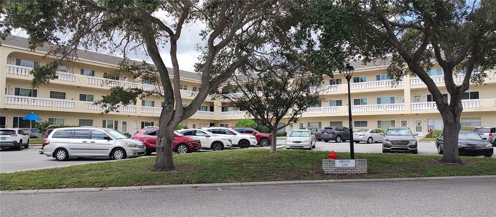 a front view of a building with trees and cars parked