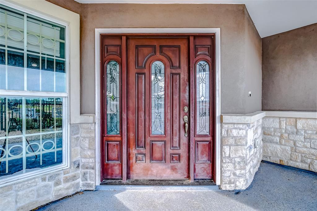 This is an inviting entryway featuring a stately red front door with elegant glass inserts, complemented by a large window and stone accents.