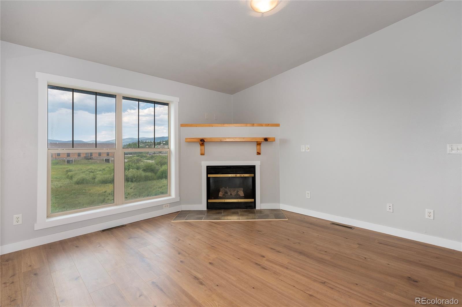 an empty room with wooden floor fire place and windows